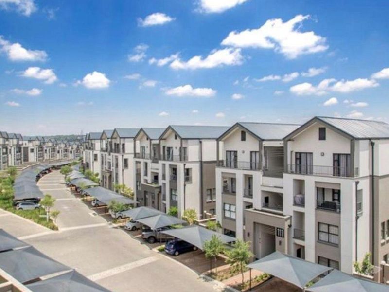 An elevated view of a modern apartment complex featuring multi-story residential buildings, paved driveways, and covered parking bays.