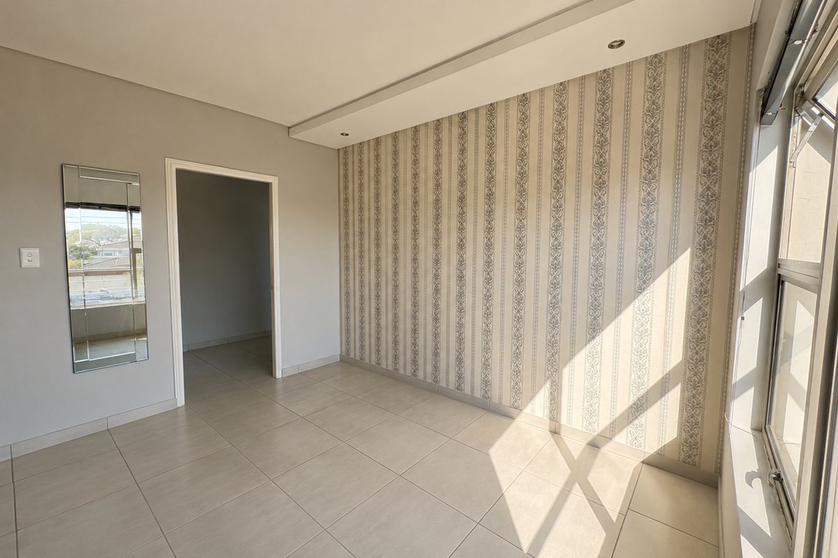 A bright, empty bedroom featuring neutral tiled flooring, a decorative feature wall, and large windows allowing for ample natural light.