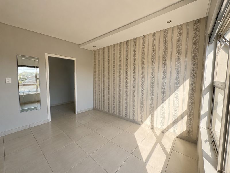 A bright, empty bedroom featuring neutral tiled flooring, a decorative feature wall, and large windows allowing for ample natural light.
