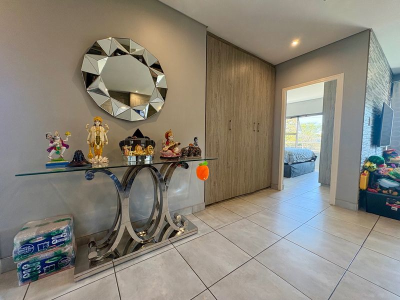 A well-maintained hallway featuring neutral tiled flooring, recessed lighting, and ample built-in cupboard storage, leading into an adjacent bedroom.