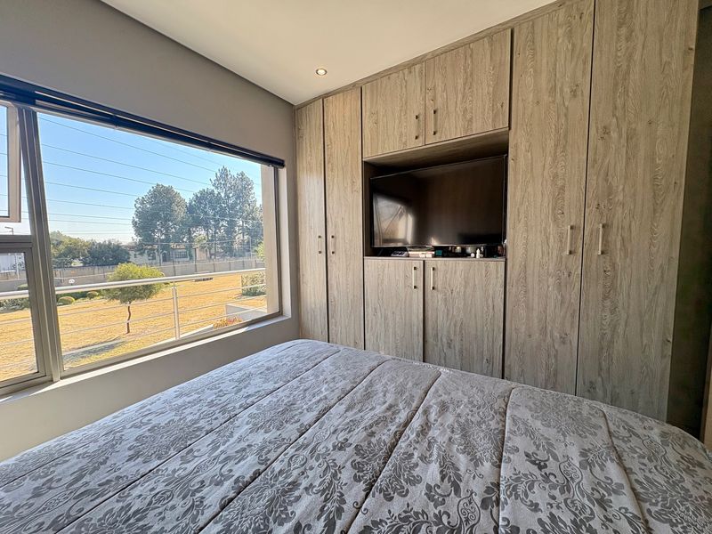 A well-lit bedroom featuring extensive built-in wooden cabinetry with integrated shelving and a large window offering an exterior view.