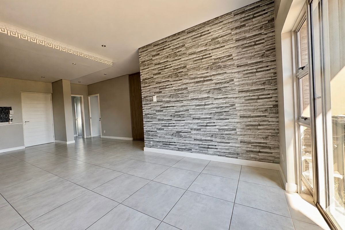 Spacious open-plan living area featuring a modern stone-cladding feature wall, large format floor tiles, and sliding glass doors leading to an outdoor space.