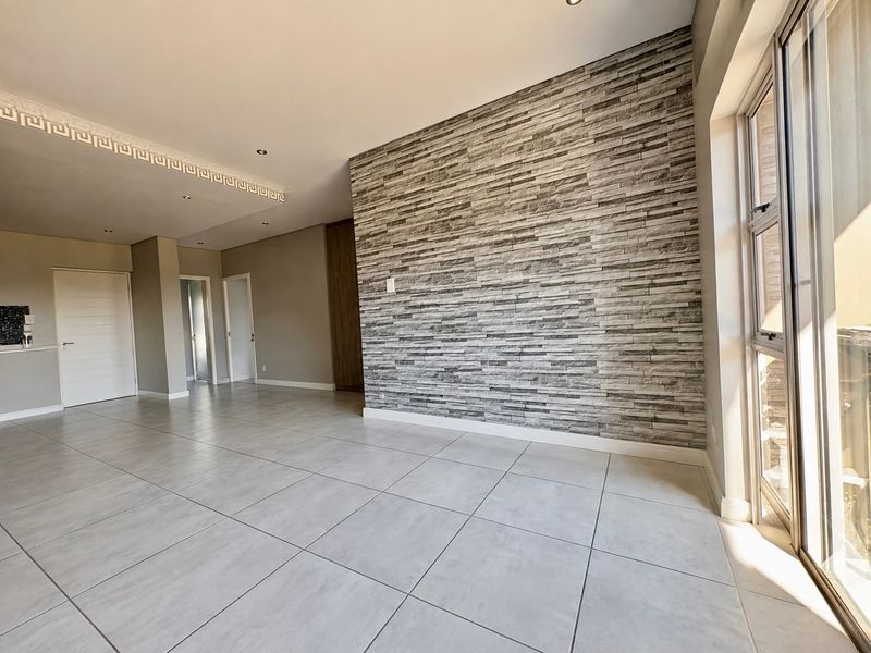 Spacious open-plan living area featuring a modern stone-cladding feature wall, large format floor tiles, and sliding glass doors leading to an outdoor space.