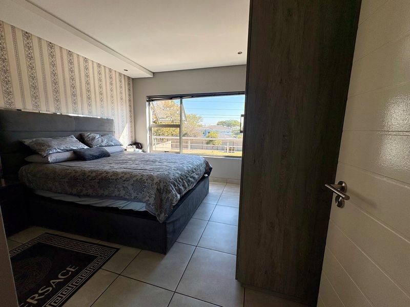 A well-maintained bedroom featuring tiled flooring, a built-in wardrobe, and large windows providing natural light and exterior views.