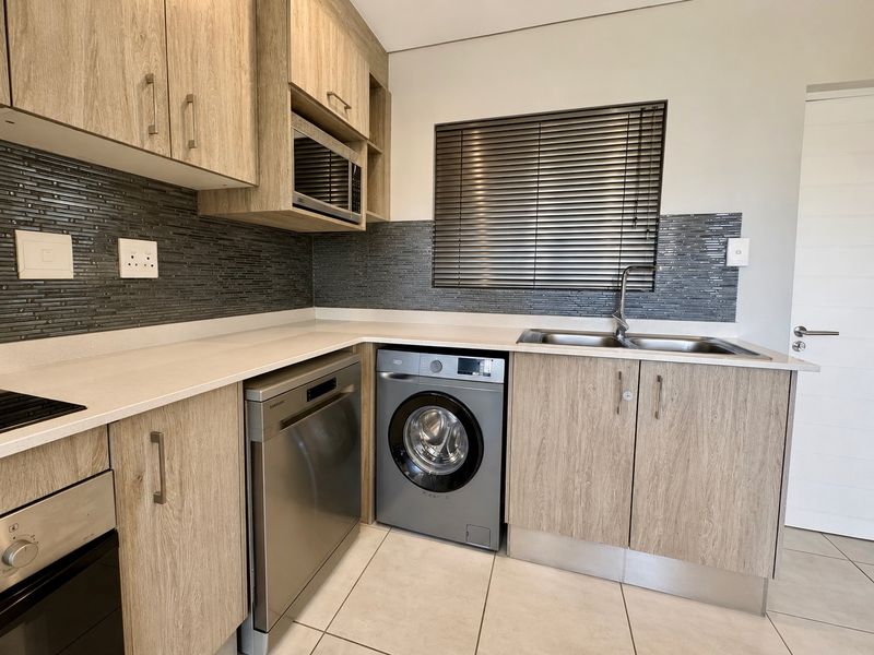 Modern kitchen featuring wood-look cabinetry, stone countertops, mosaic tile backsplash, and integrated appliances including an oven, hob, and microwave.