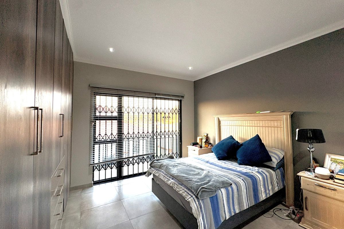 A well-maintained bedroom featuring extensive built-in cupboards, tiled flooring, recessed lighting, and a secure sliding door with integrated security gate and blinds.