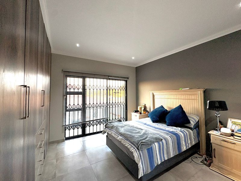A well-maintained bedroom featuring extensive built-in cupboards, tiled flooring, recessed lighting, and a secure sliding door with integrated security gate and blinds.