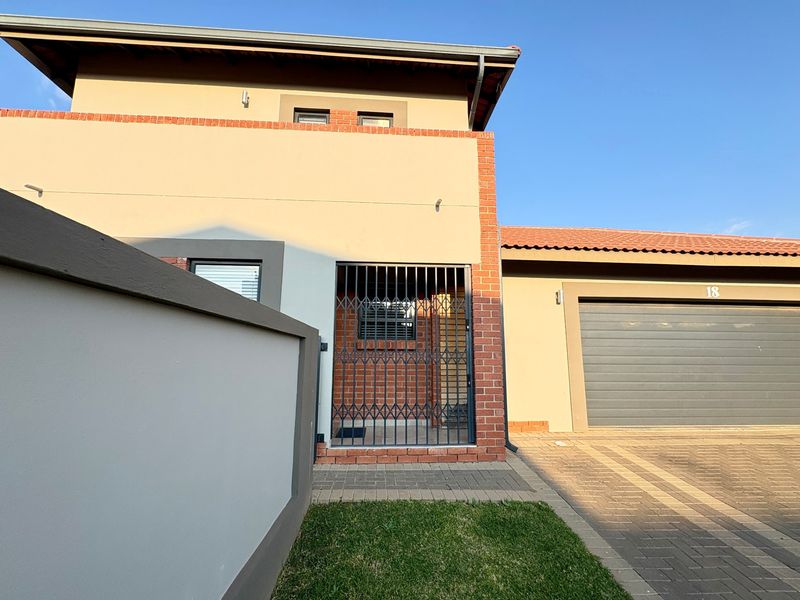 Front exterior view of a modern house featuring a brick and plaster facade, paved driveway, and an integrated garage.