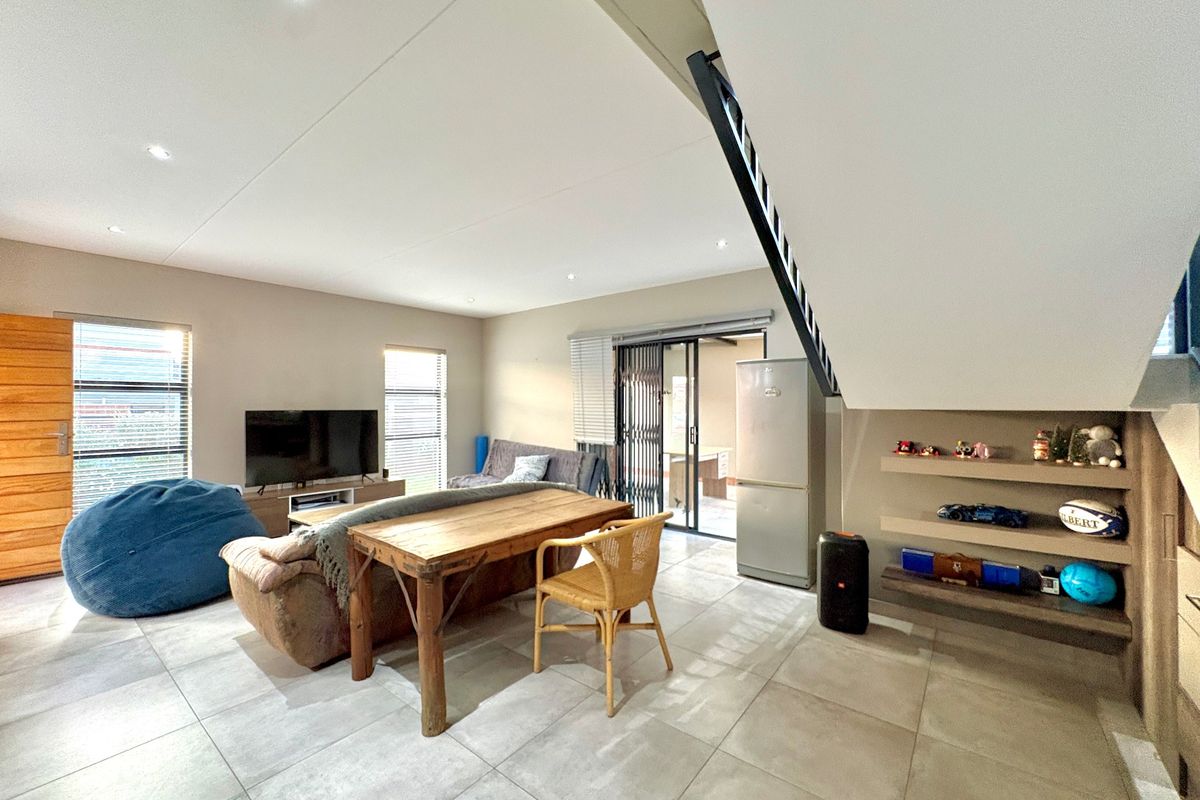 Open-plan living area featuring tiled floors, recessed lighting, and a staircase with built-in shelving underneath, leading to an outdoor patio area.