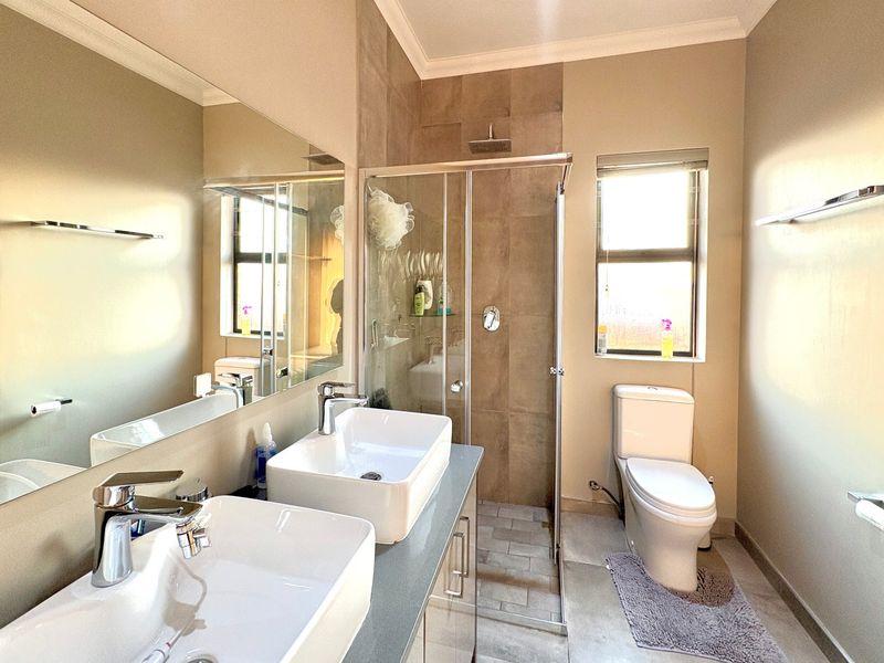 Modern bathroom featuring a double vanity with vessel sinks, a large wall mirror, and a glass-enclosed shower with a rain shower head.