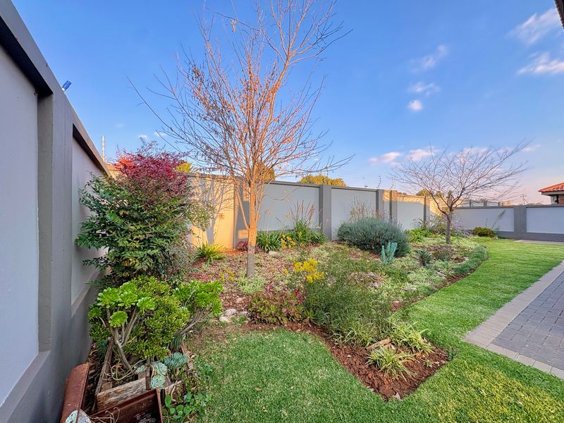 A well-maintained garden area featuring a manicured lawn, landscaped planting beds, and a secure perimeter wall with a paved walkway.