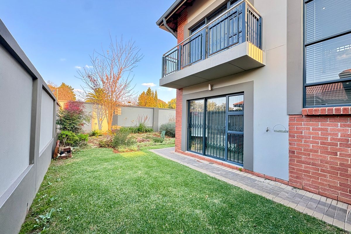 Rear view of the property featuring a manicured lawn, paved walkway, brick and rendered facade, and an upper-level balcony with metal railings.