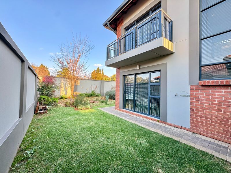 Rear view of the property featuring a manicured lawn, paved walkway, brick and rendered facade, and an upper-level balcony with metal railings.