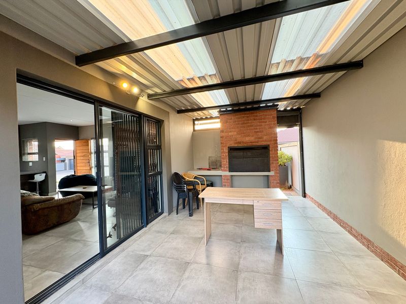 Covered patio area featuring a built-in brick braai, tiled flooring, and sliding door access to the main living space.