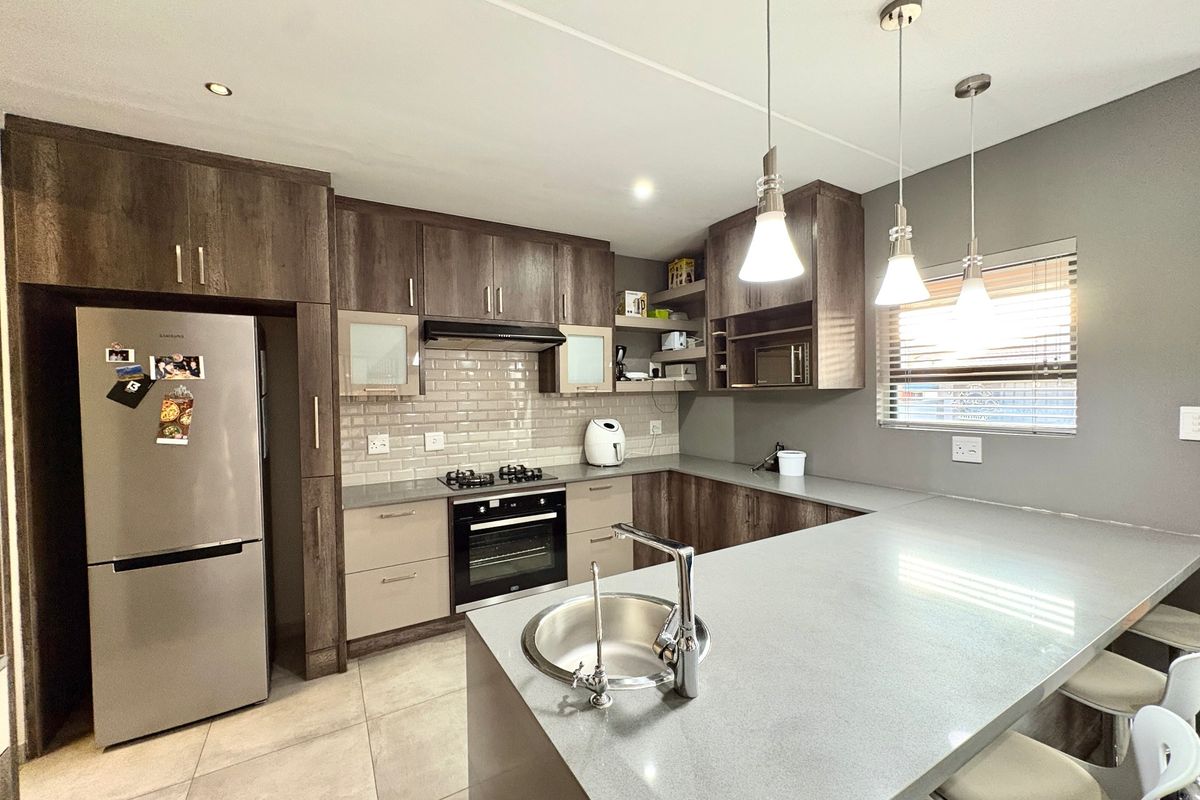 Modern kitchen featuring dark wood cabinetry, stone countertops, subway tile backsplash, integrated appliances, and a breakfast bar with pendant lighting.