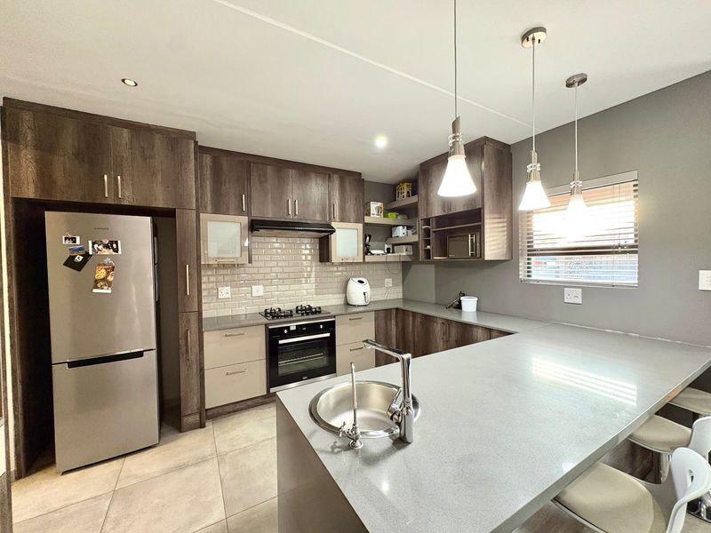 Modern kitchen featuring dark wood cabinetry, stone countertops, subway tile backsplash, integrated appliances, and a breakfast bar with pendant lighting.