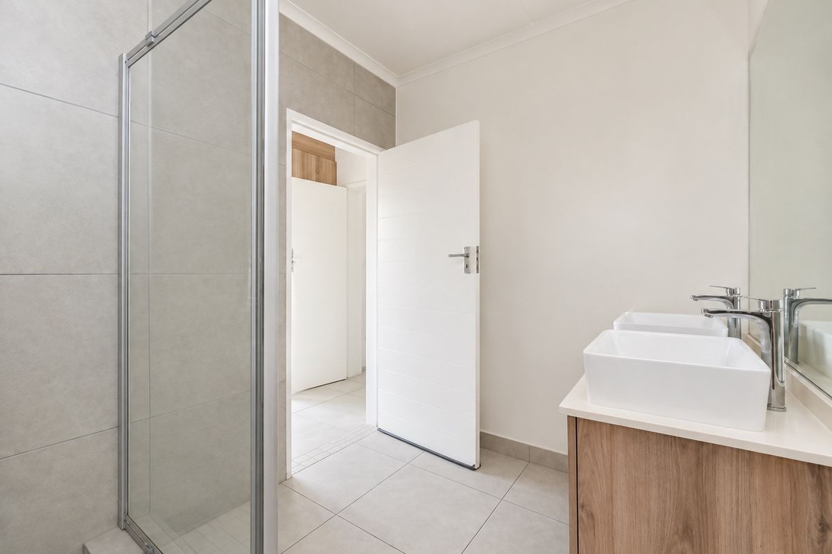 Modern bathroom featuring a glass shower enclosure, double vanity with vessel sinks, chrome fixtures, and neutral wall and floor tiling.