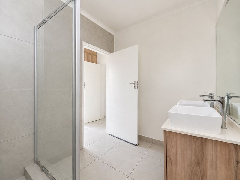 Modern bathroom featuring a glass shower enclosure, double vanity with vessel sinks, chrome fixtures, and neutral wall and floor tiling.