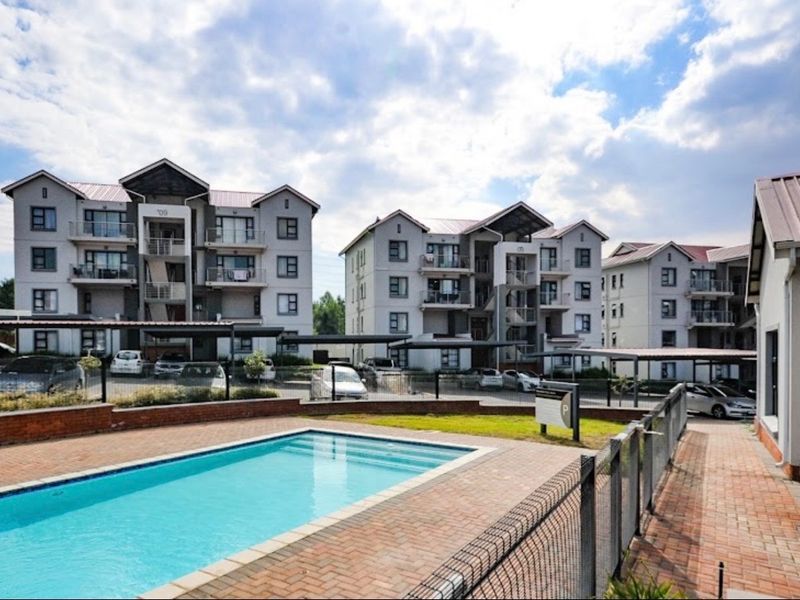 A well-maintained apartment complex featuring a communal swimming pool, brick-paved surrounds, and dedicated covered parking bays for residents.