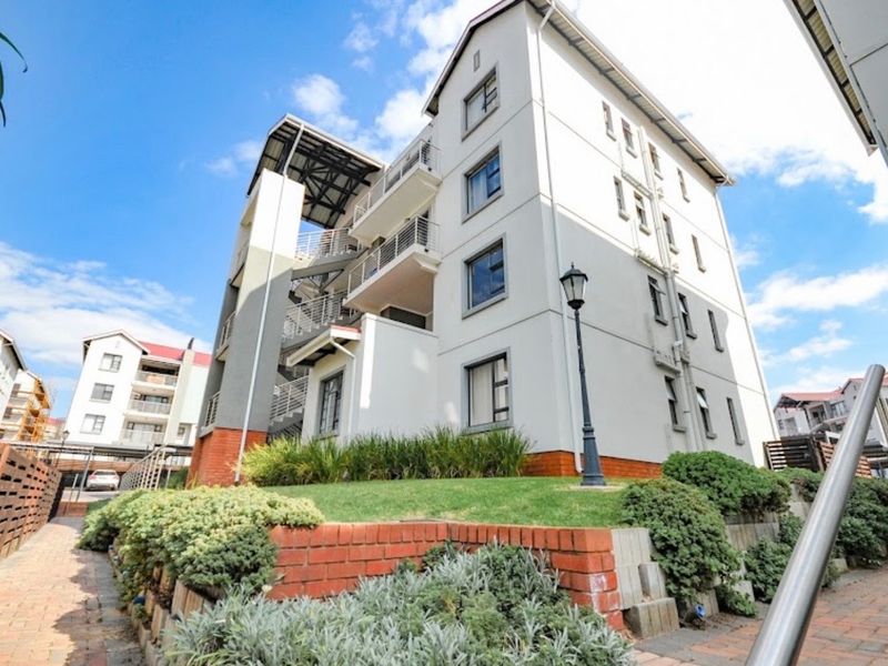 Exterior view of a multi-story apartment building featuring brick retaining walls, landscaped garden beds, and external staircases.