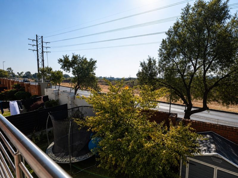 Elevated balcony view overlooking a private garden area with brick boundary walls and surrounding neighborhood landscape.