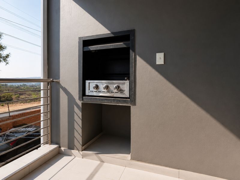 A modern balcony featuring a built-in stainless steel braai, tiled flooring, and a sleek stainless steel balustrade with scenic views.