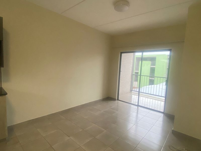 An empty open-plan living area featuring tiled flooring, built-in kitchen cabinetry with granite countertops, and a sliding glass door leading to a balcony.