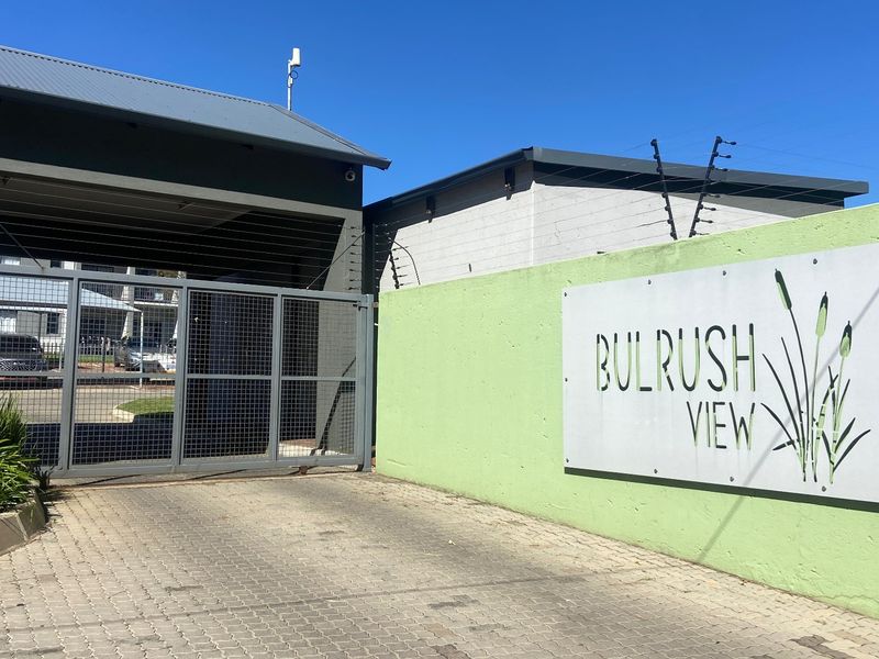 The entrance to Bulrush View apartment complex, featuring a secure gated access point, paved driveway, and perimeter electric fencing.