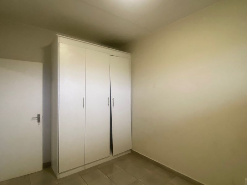 A simple, empty bedroom featuring neutral tiled flooring and a white built-in wardrobe with three doors.