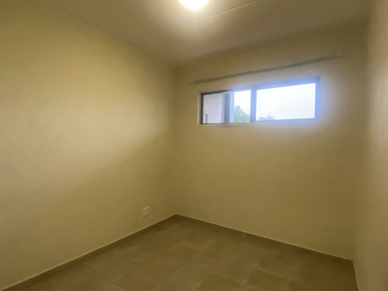 A simple, empty bedroom featuring neutral wall finishes, tiled flooring, and a horizontal window providing natural light.