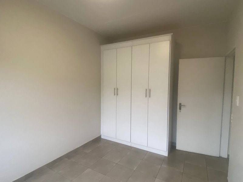A clean, empty bedroom featuring neutral tiled flooring and a white built-in wardrobe, offering a blank canvas for personalization.
