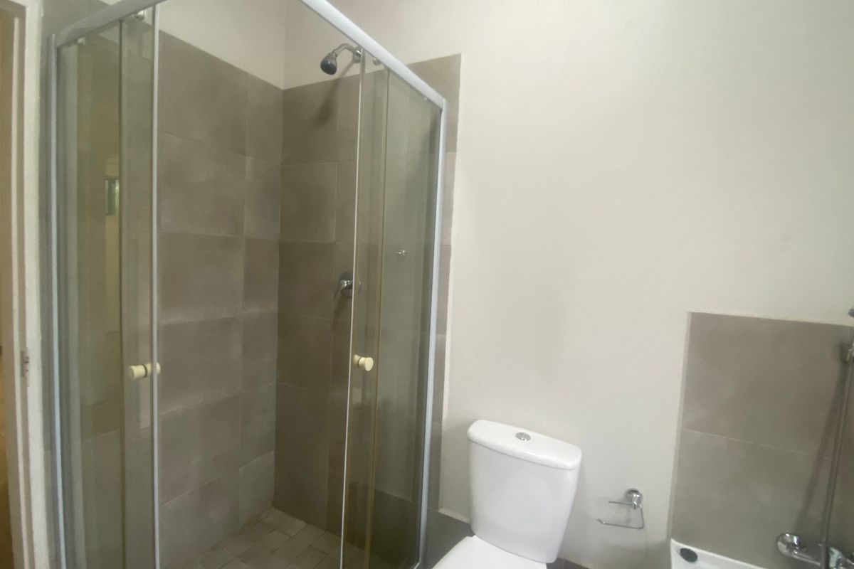 A functional bathroom featuring a glass-enclosed shower, a standard toilet, and neutral wall tiling.