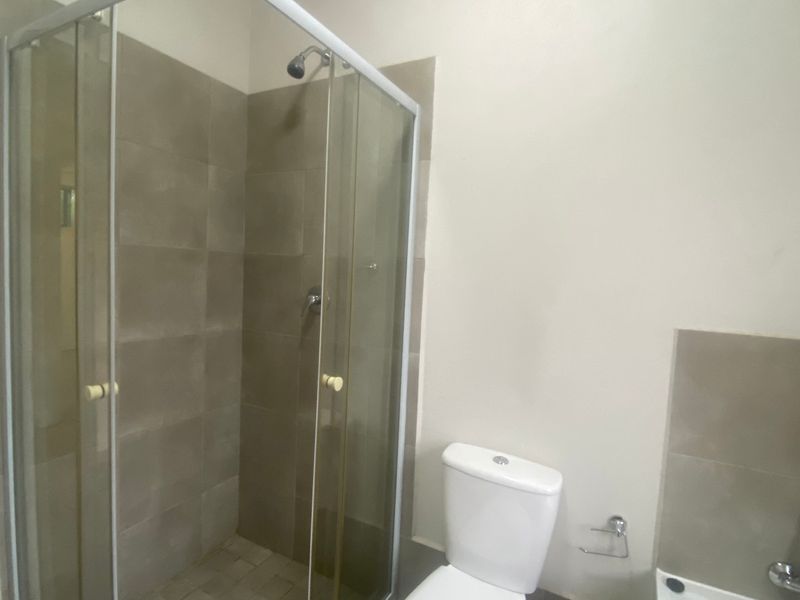 A functional bathroom featuring a glass-enclosed shower, a standard toilet, and neutral wall tiling.