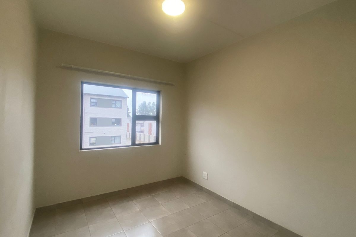 A clean, empty bedroom featuring neutral tiled flooring, a ceiling light fixture, and an aluminium-framed window providing natural light.