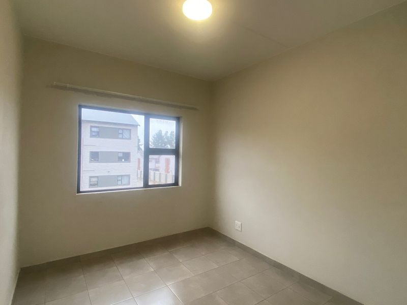 A clean, empty bedroom featuring neutral tiled flooring, a ceiling light fixture, and an aluminium-framed window providing natural light.