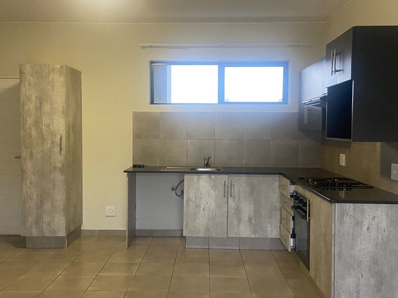 A functional kitchen featuring modern grey-toned cabinetry, dark countertops, a built-in oven with gas hob, and tiled flooring throughout.