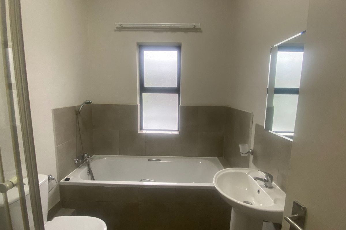 A functional bathroom featuring a bathtub with shower mixer, pedestal basin, and toilet, finished with neutral wall tiling and a frosted window.