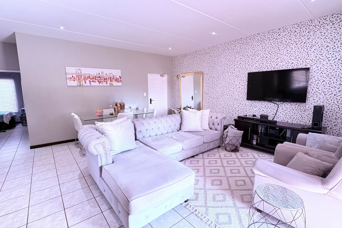 A well-maintained living room featuring tiled flooring, recessed ceiling lights, and a distinct patterned feature wall, creating a comfortable and functional living space.
