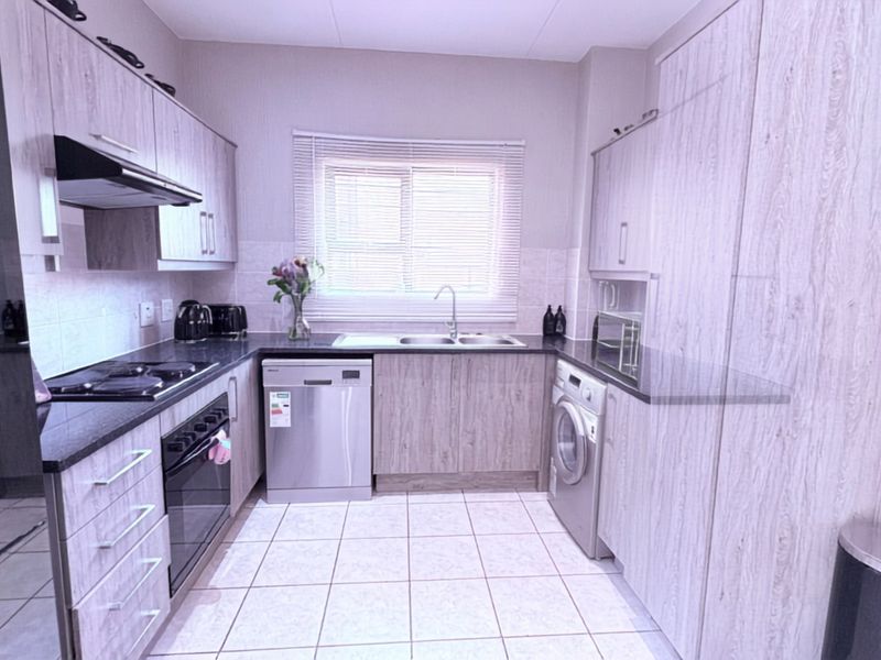 A functional kitchen featuring light wood-grain cabinetry, dark granite countertops, tiled flooring, and integrated appliances including an oven, hob, and extractor fan.
