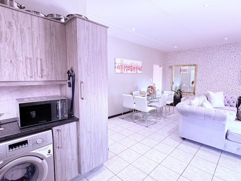 Open-plan living area featuring a modern kitchen with built-in cabinetry, integrated laundry appliances, and tiled flooring throughout the dining and lounge space.