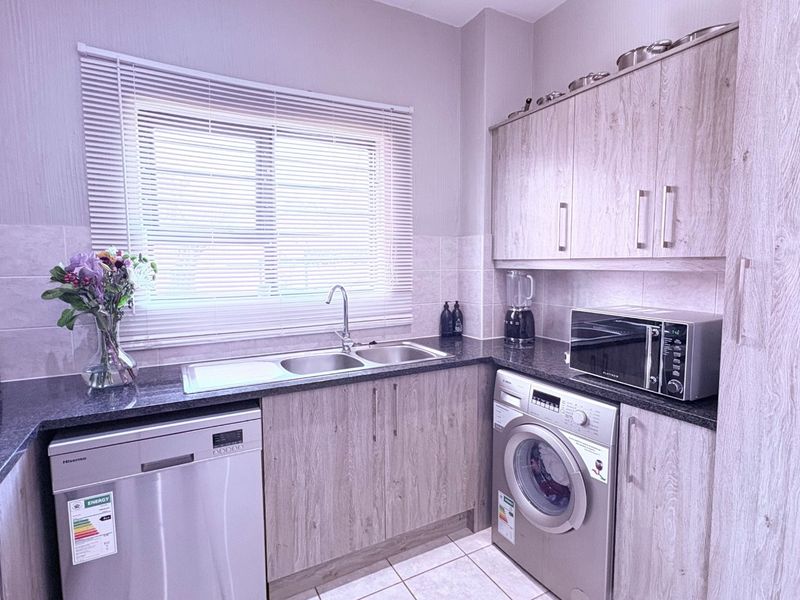 Modern kitchen featuring light wood-grain cabinetry, dark granite countertops, tiled backsplash, and integrated appliances including a dishwasher and washing machine.