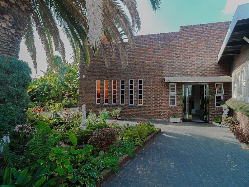 Front elevation of a face brick house featuring a paved driveway, established garden, and secure entrance with window security bars.