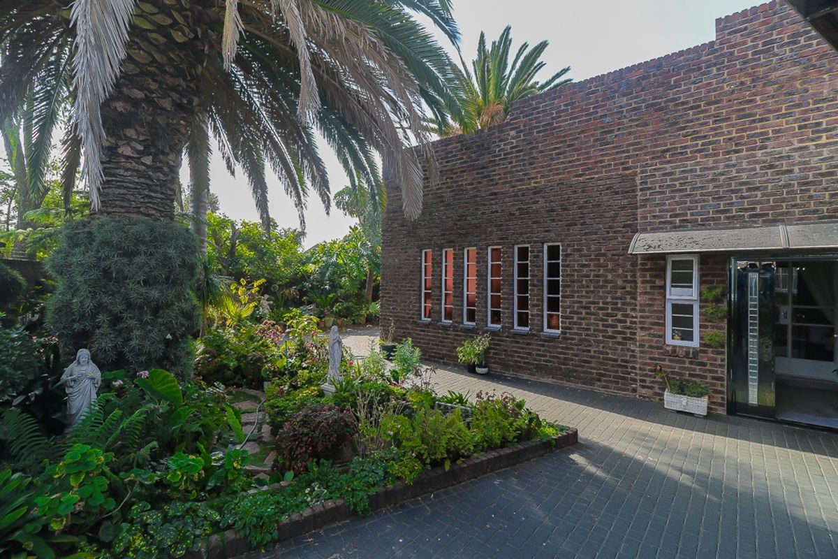 A rear exterior view featuring an exposed brick facade, paved patio area, and established garden with mature palm trees.