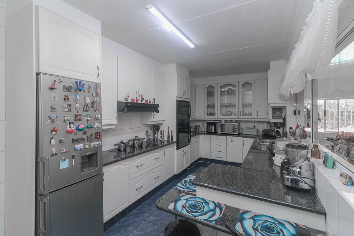 A functional kitchen featuring white cabinetry, dark granite countertops, built-in oven, electric hob, and a breakfast bar area with tiled flooring.