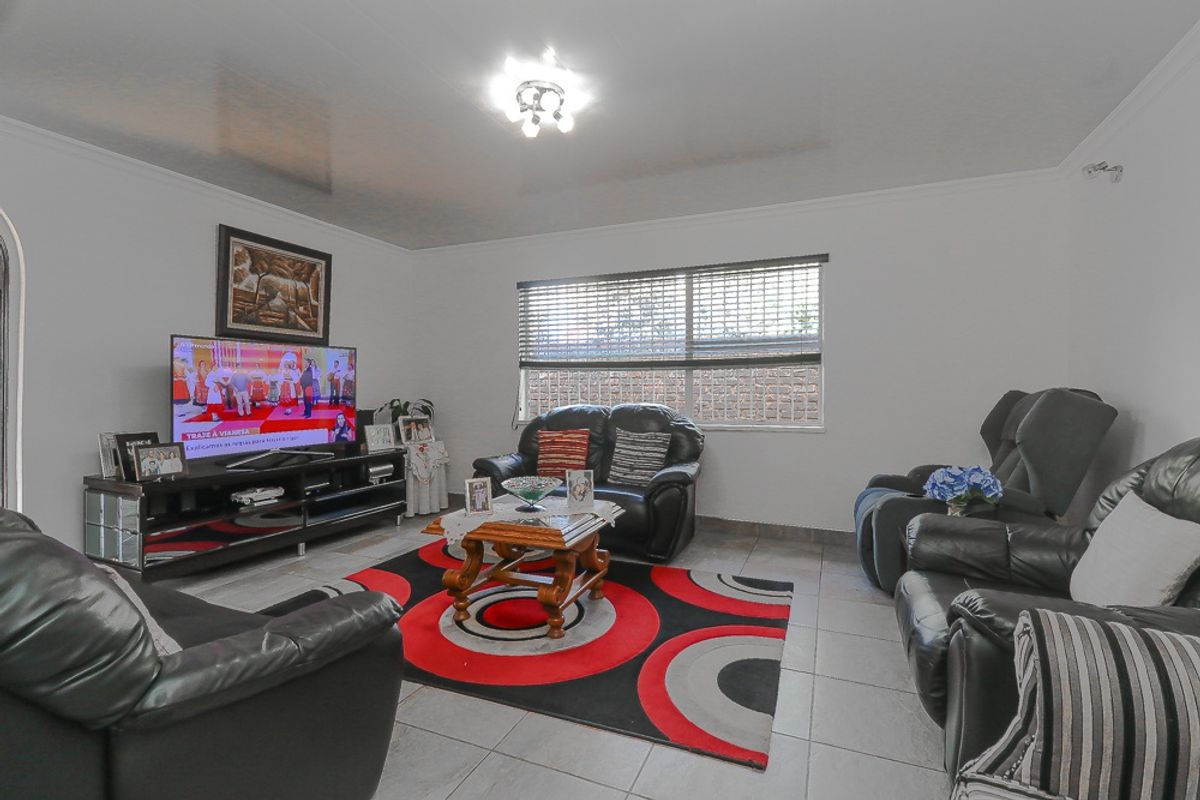 A well-maintained living room featuring neutral tiled flooring, coved ceilings, and large windows with venetian blinds, providing a bright and functional living space.