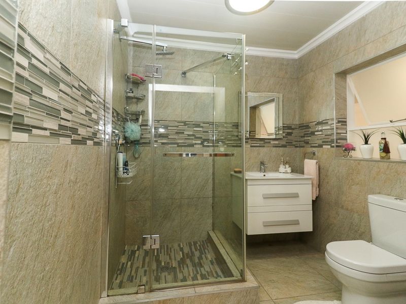Modern bathroom featuring a glass-enclosed shower, wall-mounted vanity with basin, and neutral stone-look tiling throughout.