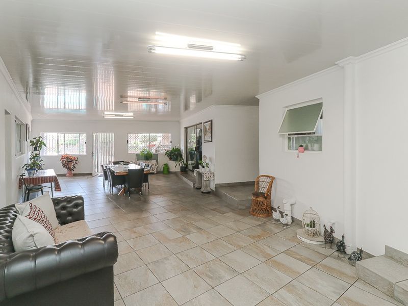 Spacious open-plan living and dining area featuring large format floor tiles, a glossy ceiling finish, and ample natural light through multiple windows.