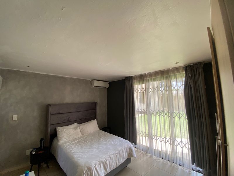 A bedroom featuring tiled flooring, an air conditioning unit, and a sliding glass door with a security gate leading to the exterior.
