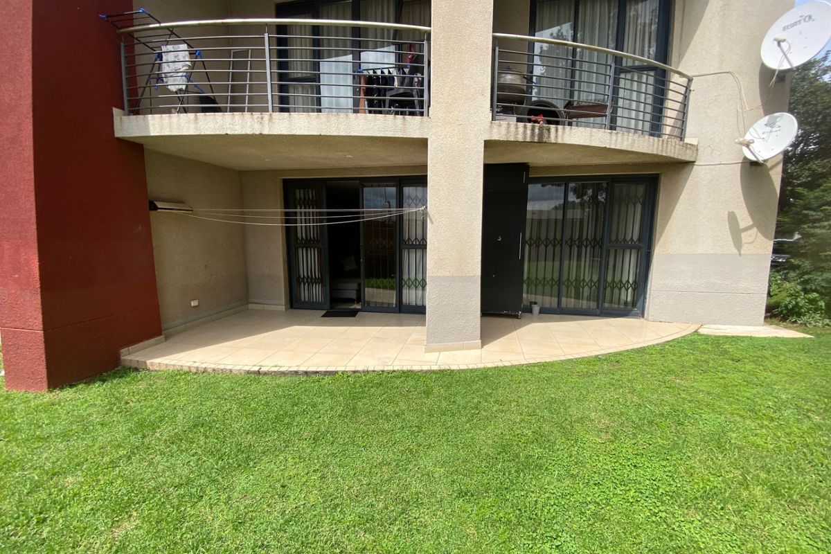 Rear view of the apartment building featuring a ground floor tiled patio and an upper level balcony with stainless steel balustrades.