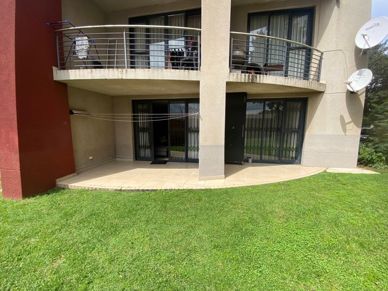 Rear view of the apartment building featuring a ground floor tiled patio and an upper level balcony with stainless steel balustrades.
